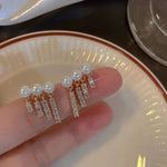 Pearl Crystal Bar Tassel Drop Earrings — held in hand on white ceramic plate showing two pairs with faux pearl studs and triple crystal bar tassel drops in gold-colored finish