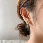 Crystal Bow Ribbon Tassel Drop Earrings — held in hand showing pair with fully pavé zirconia bow and triple crystal tassel drops in gold-colored finish