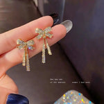 Crystal Bow Ribbon Tassel Drop Earrings — held between fingers showing pair with sparkling AD crystal bow and dangling rhinestone tassel chains