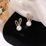 Pearl bunny stud earrings on dark reflective surface — close up